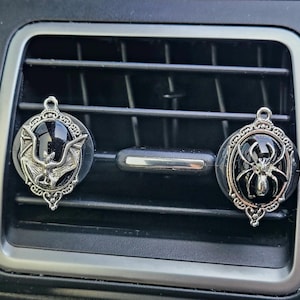 May include: Two silver car air freshener charms with black glass inserts. One charm features a silver bat silhouette and the other features a silver spider silhouette.