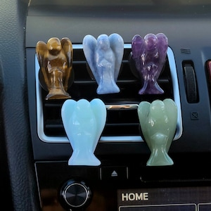 Könnte beinhalten: Sechs Kristall-Engel-Auto-Lüftungsgitterclips in verschiedenen Farben, darunter Braun, Blau, Lila, Grün und Weiß. Die Engel sind in einer Reihe auf einem Auto-Lüftungsgitter angeordnet.