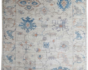 May include: A beige rug with a blue, orange, and gray geometric pattern. The rug has a traditional design with intricate details.
