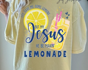 May include: Butter-colored t-shirt with a graphic design. The design features a lemon slice, a glass of lemonade with pink straws, and the text "Life gave me some lemons but my Jesus he be makin' lemonade."