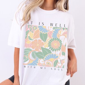 May include: White t-shirt with a floral design and the text "It is well with my soul".