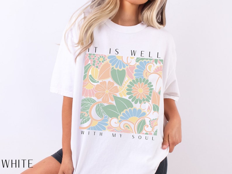 May include: White t-shirt with a floral design and the text "It is well with my soul".