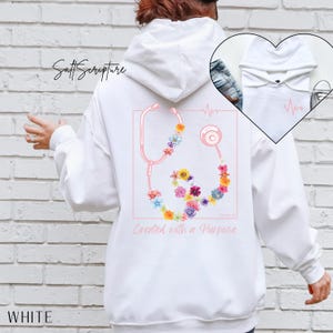 May include: White hoodie featuring a pink stethoscope design adorned with colorful flowers. The text "Created with a Purpose" is below the stethoscope. The word "WHITE" is printed at the bottom.