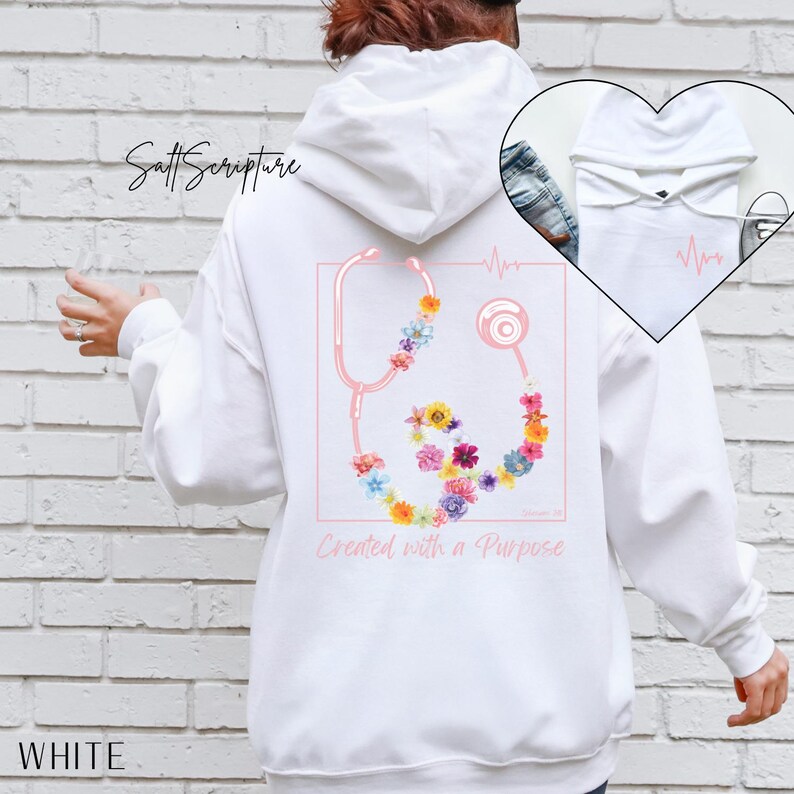 May include: White hoodie featuring a pink stethoscope design adorned with colorful flowers. The text "Created with a Purpose" is below the stethoscope. The word "WHITE" is printed at the bottom.