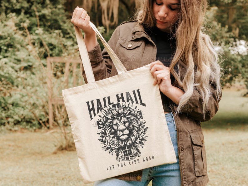 May include: A beige tote bag with black text and a graphic of a lion's head with a crown. The text on the bag reads "Hail Hail Lion of Judah Let the Lion Roar".