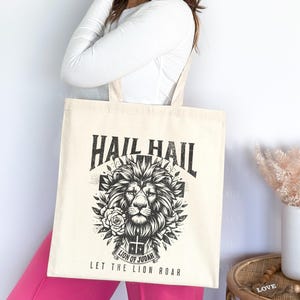 May include: A white tote bag with a black and white graphic of a lion's head with the text "Hail Hail Let the Lion Roar" and "Lion of Judah" printed on it.