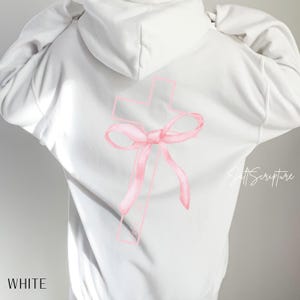 May include: White hoodie with a pink cross and bow design on the back. The word "WHITE" is printed at the bottom. The hoodie has a drawstring hood and long sleeves. The design is a watercolor style.