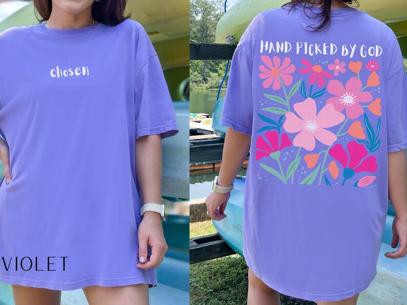 May include: Violet-colored t-shirt with the word "chosen" in white on the front. The back of the shirt features a floral design with the text "HAND PICKED BY GOD". The flowers are pink, orange, and blue.