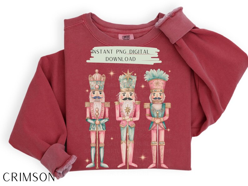 May include: A red sweatshirt with a graphic of three nutcracker soldiers. The nutcrackers are wearing pink and blue uniforms and holding swords. The text "INSTANT PNG DIGITAL DOWNLOAD" is printed on the sweatshirt.