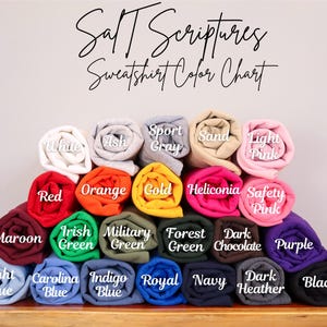 May include: A color chart showing the different sweatshirt colors available. The colors include white, ash, sport gray, sand, light pink, red, orange, gold, heliconia, safety pink, maroon, irish green, military green, forest green, dark chocolate, purple, light blue, carolina blue, indigo blue, royal blue, navy, dark heather, and black.
