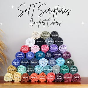 May include: A display of rolled fabric swatches in various colors, including white, black, blue, green, red, orange, yellow, and purple. The fabric swatches are arranged in a pyramid shape and labeled with color names. The text "Salt Scriptures Comfort Colors" is at the top of the image.