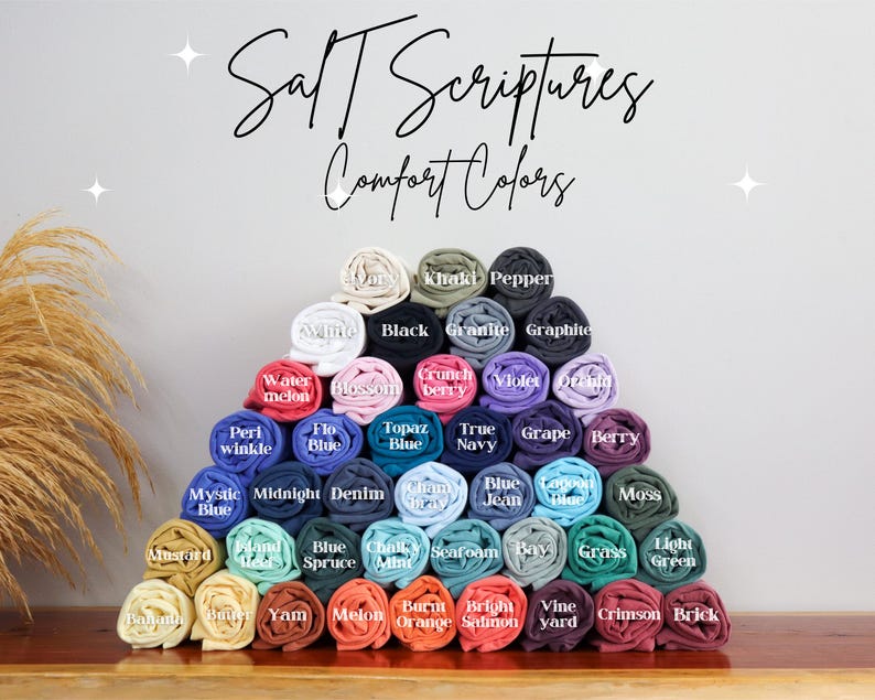 May include: A display of rolled fabric swatches in various colors, including white, black, blue, green, red, orange, yellow, and purple. The fabric swatches are arranged in a pyramid shape and labeled with color names. The text "Salt Scriptures Comfort Colors" is at the top of the image.