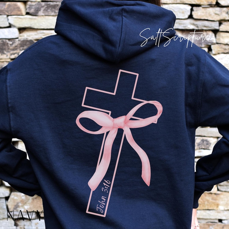 May include: Navy blue hoodie featuring a pink cross design with a bow and the text "John 3:16." The hoodie has a hood and long sleeves. The words "Salt Scripture" are written in cursive on the upper right side of the hoodie.