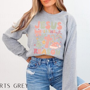 May include: A gray sweatshirt with a Christmas-themed graphic that says "Jesus is the reason for the season".