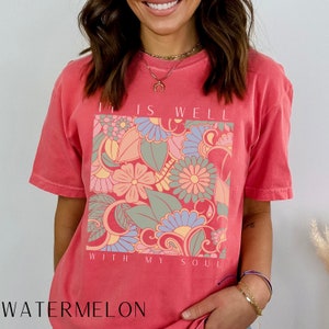 May include: A pink t-shirt with a floral design and the text "It is well with my soul".