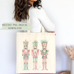May include: A white tote bag with a design of three watercolor nutcracker soldiers. The nutcrackers are wearing pink, green, and blue uniforms with gold accents. The bag has the text "INSTANT PNG DIGITAL DOWNLOAD" at the top.