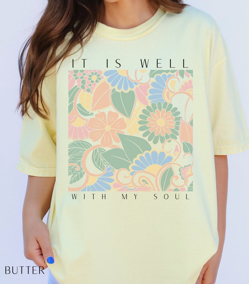 May include: A yellow t-shirt with a floral design and the text "It is well with my soul".