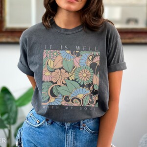 May include: A charcoal grey t-shirt with a floral design and the text "It is well with my soul".