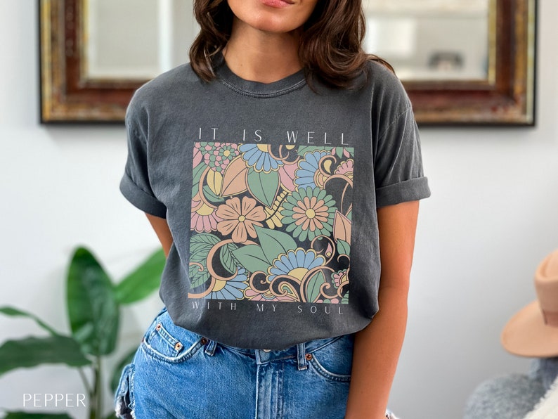 May include: A charcoal grey t-shirt with a floral design and the text "It is well with my soul".