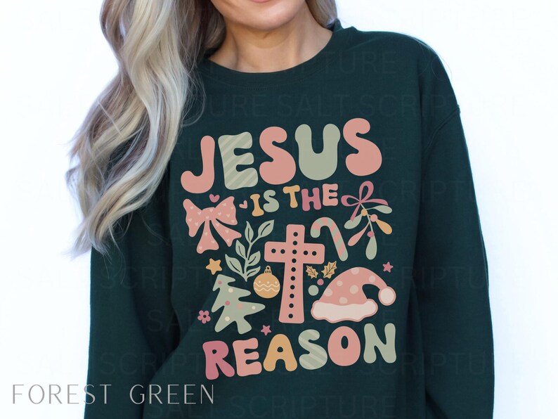 May include: Forest green sweatshirt with a Christmas-themed graphic that says "Jesus is the reason" with a cross, a bow, a candy cane, and a Christmas tree.