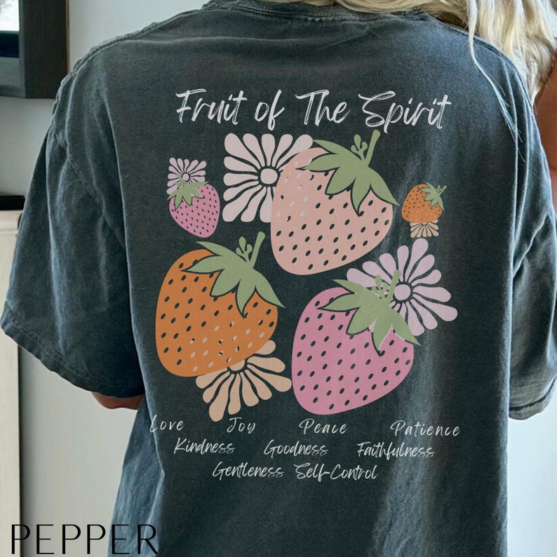 May include: A dark gray t-shirt with the text "Fruit of The Spirit" printed in white. The shirt features a design of strawberries and flowers with the words "Love, Joy, Peace, Patience, Kindness, Goodness, Faithfulness, Gentleness, Self-Control" printed in white around the design.