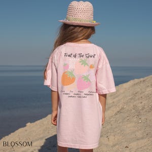 May include: A pink t-shirt with a graphic of strawberries and the text "Fruit of The Spirit". The text below the graphic lists the fruits of the spirit: love, joy, peace, patience, kindness, goodness, faithfulness, gentleness, and self-control.