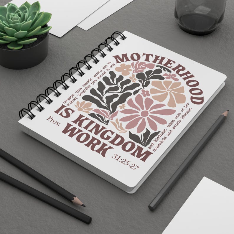 May include: A white spiral notebook with a floral design and the text "MOTHERHOOD IS KINGDOM WORK Prov. 31:25-27".