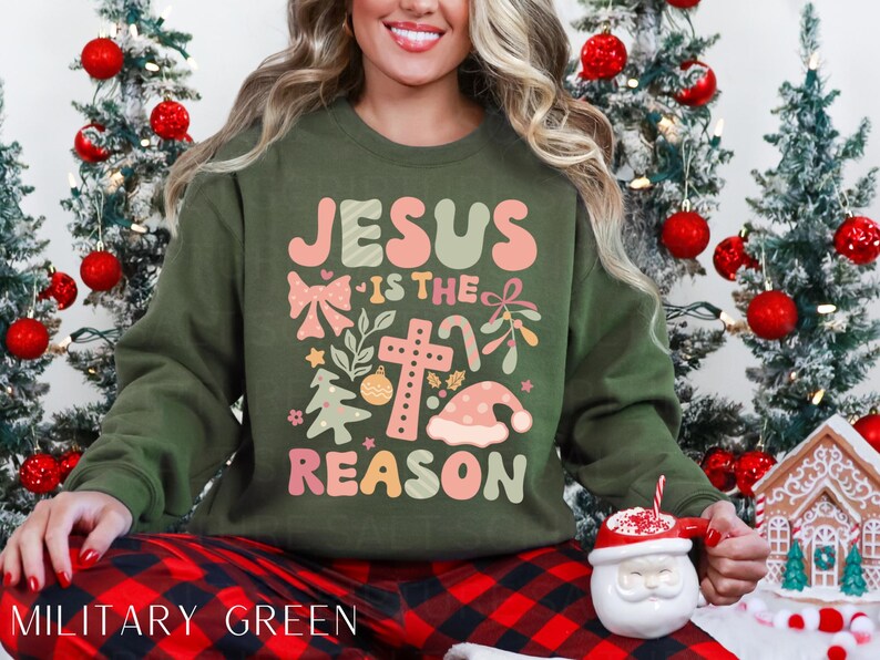 May include: A green Christmas sweatshirt with the text "Jesus is the reason" in pink and white lettering. The design includes a cross, a bow, and a Christmas tree.