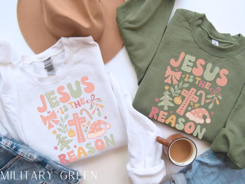 May include: Two Christmas sweatshirts with the text "Jesus is the reason" in a colorful, festive font. The sweatshirts are white and military green.