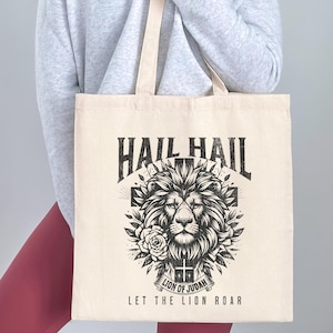 May include: A white canvas tote bag with a black and white graphic design featuring a lion's head with a cross and the text "Hail Hail Lion of Judah Let the Lion Roar".