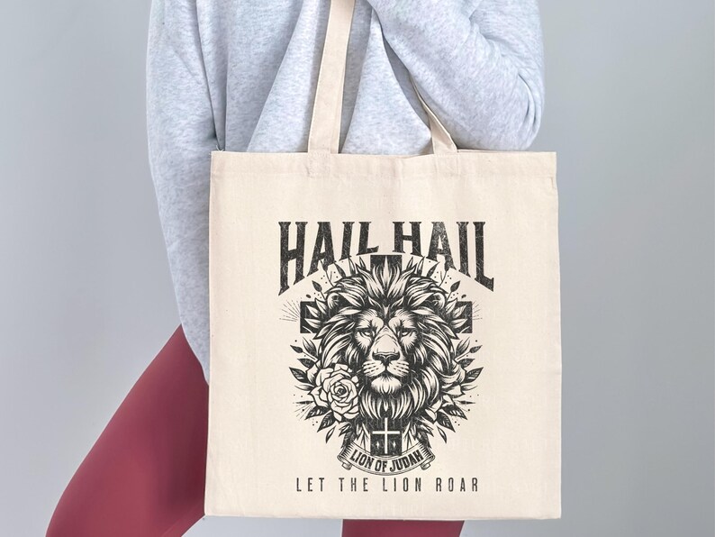 May include: A white canvas tote bag with a black and white graphic design featuring a lion's head with a cross and the text "Hail Hail Lion of Judah Let the Lion Roar".