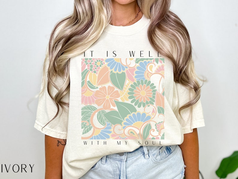 May include: A cream coloured t-shirt with a floral design and the text "It is well with my soul".