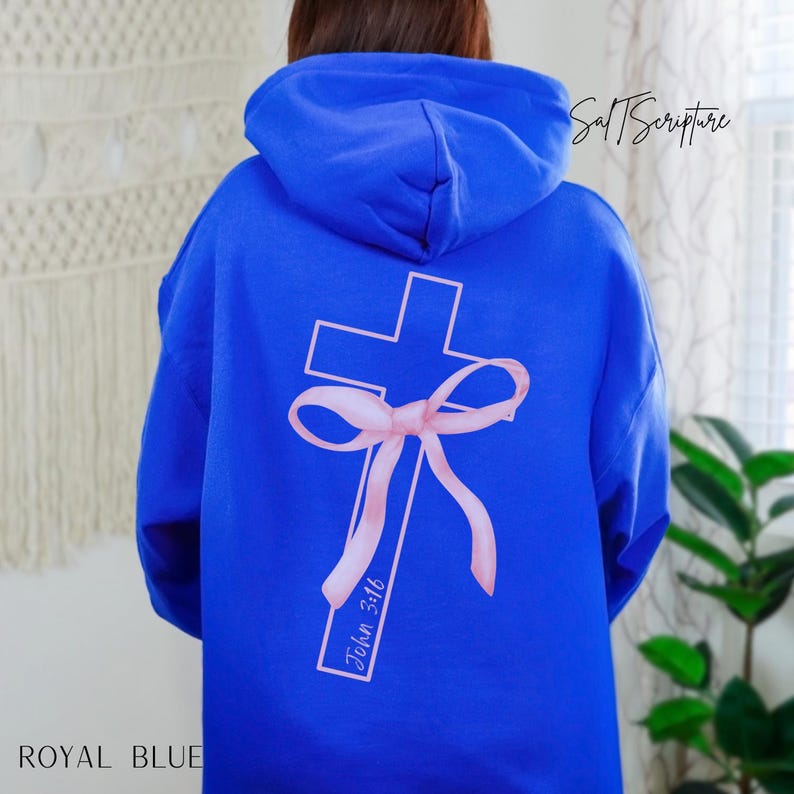 May include: Royal blue hoodie with a cross and bow design on the back. The cross is light pink with a matching bow and the text "John 3:16". The hoodie has a hood and long sleeves.