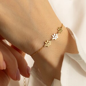 May include: A gold chain bracelet with three paw print charms. Each charm has a small inscription.