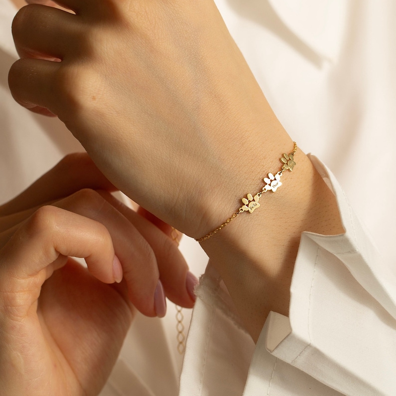 May include: A gold chain bracelet with three paw print charms. Each charm has a small inscription.