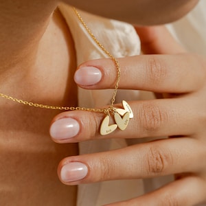 Könnte beinhalten: Eine goldfarbene Halskette mit drei herzförmigen Anhängern. Jeder Anhänger trägt einen eingravierten Namen: Ava, Lily und Nancy. Die Halskette hat eine feine Kette.