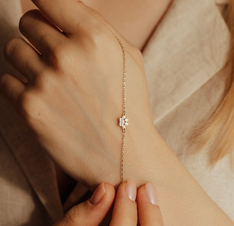 May include: A delicate gold chain bracelet with a small paw print charm. The charm has a single clear stone in the center.