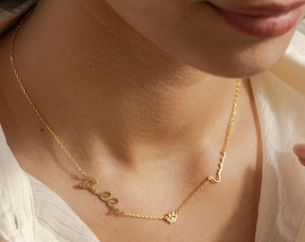 May include: A delicate gold necklace featuring the name "Bella" in cursive script, a paw print charm, and a heartbeat symbol. The necklace is worn around the neck, showcasing its elegant design and personalized touch. The jewelry is a stylish accessory.