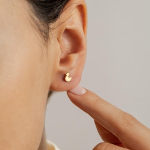 May include: A close-up of a person's ear with a small gold duck earring. The earring is a simple design with a rounded shape.