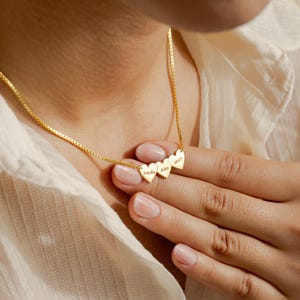 May include: Gold necklace with three heart-shaped charms, each engraved with a name: Amelia, John, and Mary.
