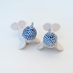 May include: Two white ceramic narwhal figurines with blue and white polka dot patterns on their backs. Each narwhal has a white, spiraled horn.