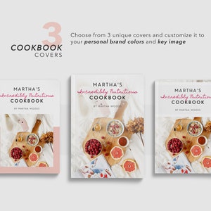 May include: Three different cookbook cover designs featuring a white background with the title "Martha's Incredibly Nutritious Cookbook" in pink script. Each cover features a photograph of a wooden tray with a bowl of granola, raspberries, a grapefruit, and a cup of tea.