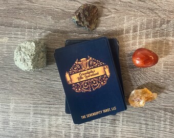 May include: A deck of cards with a blue background and gold lettering. The text on the cards reads "Serendipity's Little Lenormand" and "The Serendipity Tarot, LLC".