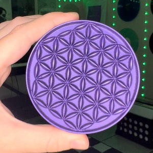 May include: A purple round coaster with a raised geometric pattern resembling a flower of life.