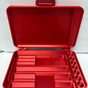 May include: A bright red, open storage case featuring a hinged lid and a molded interior. The base contains various rectangular compartments of different sizes and a vertical row of six circular slots designed for organizing small items.