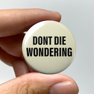 May include: A white button with black text that reads "DONT DIE WONDERING".