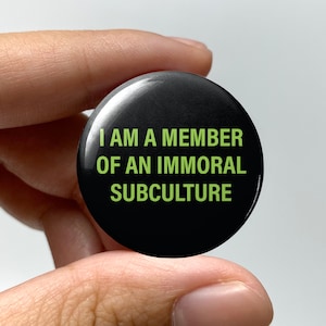 May include: Black button with the text "I AM A MEMBER OF AN IMMORAL SUBCULTURE" in green letters.