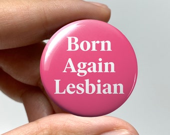 May include: Pink button with white text that reads "Born Again Lesbian".