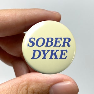 May include: A yellow button with blue text that reads "SOBER DYKE".