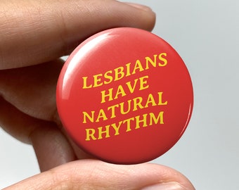 May include: A red button with the text "Lesbians Have Natural Rhythm" in yellow letters.